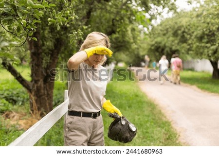 woman wearing latex gloves picking up litter to garbage bag, holding used plastic bottle in hand, takes care of planet