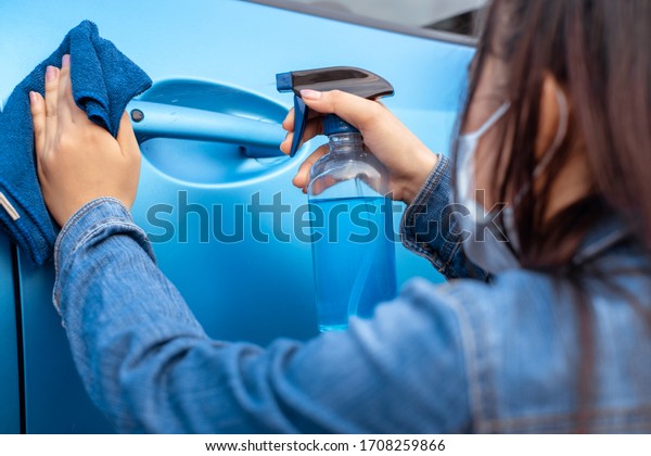 Woman wearing\
mask cleaning car door handle socket with alcohol spray protection\
germs, virus and bacteria coronavirus,covid-19 health care,\
Transportation protective\
concept.