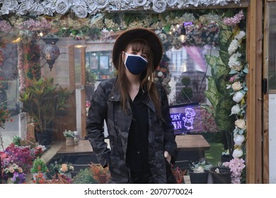woman wearing a mask and hat waiting outside a coffee shop in the city