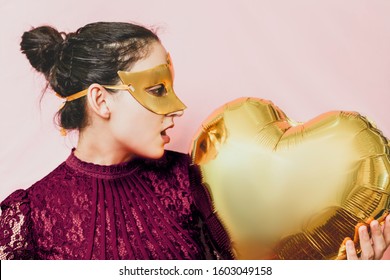 Woman Wearing Masquerade Mask And Holding Heart Shaped Air Ballon. Valentines Day, Birthday, Anniversary, Festive, Ball Celebration Concepts. Attractive Female Getting Prepared For Masquerade Party