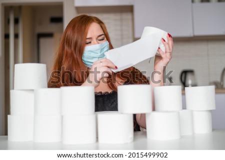 Woman wearing medical mask and holding several rolls of toilet paper.