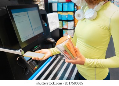 woman wearing medical mask scans her supermarket purchases at self-service checkout to make it safer to avoid contact with sellers and cash during covid pandemic