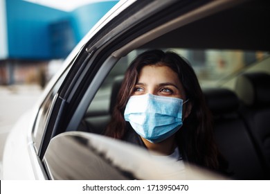 A woman wearing a medical sterile mask in a taxi car on a backseat looking sideway out of open window. Girl passenger waiting in a traffic jam during coronavirus quarantine. Healthcare safety concept