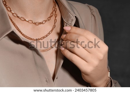 Woman wearing metal chains on grey background, closeup. Luxury jewelry