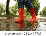 Woman wearing orange rubber boots walking in puddle outdoors, closeup