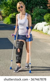 Woman Wearing An Orthopedic Leg Brace With Adjustable Straps To Immobilise Her Leg Following Surgery Or An Accident Walking On Crutches Outdoors