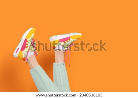 Woman wearing pair of new stylish sneakers on orange background, closeup. Space for text