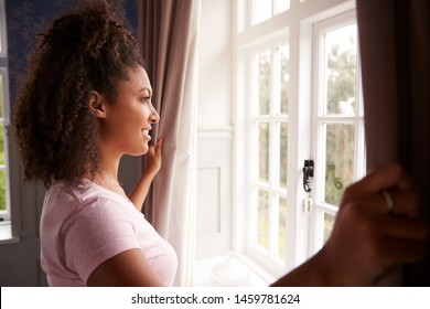 Woman Wearing Pajamas Opening Bedroom Curtains At Start Of New Day