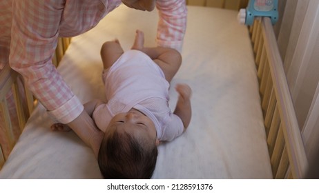 Woman Wearing Pajamas Is Picking Her Young Child From The Baby Bed Carefully In Night Time At Home Alone