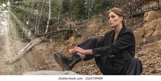 Woman Wearing Pantsuit Sits On A Mountain And Ties Her Ankle Boots. Autumn Fashion Collection. Fashionable Black Leather Shoes. Street Style