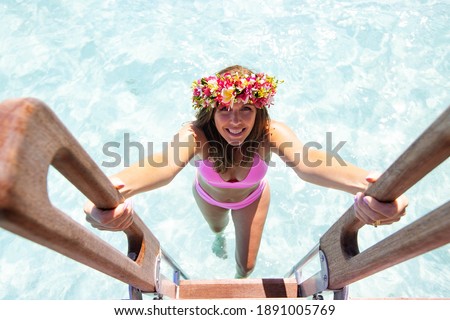 Woman wearing pink bikini and a colorful flower crown climbs a l