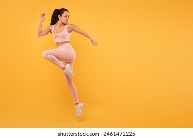 A woman wearing a pink outfit is captured mid-air as she jumps. Her joyful expression is evident as she defies gravity. The background is blurred, emphasizing her movement, copy space - Powered by Shutterstock