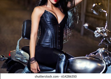Woman wearing professional waist training black leather corset sits on a bike