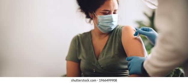 Woman Wearing Protective Face Mask Getting Vaccine Shot At Home. Female Receiving Covid Vaccination By A Healthcare Worker At Home.