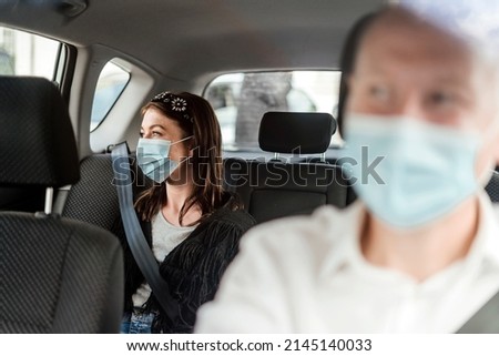 A woman wearing a protective mask on the back seat of a taxi car