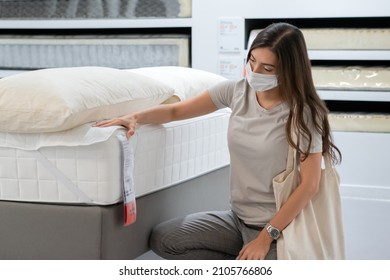 Woman Wearing Protective Mask Selecting Bed Mattress For Moving Home Or Decorate New Room. New Normal Shopping During Coronavirus Pandemic.