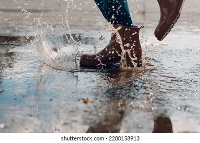 Woman Wearing Rain Rubber Boots Walking Running And Jumping Into Puddle With Water Splash And Drops In Autumn Rain.