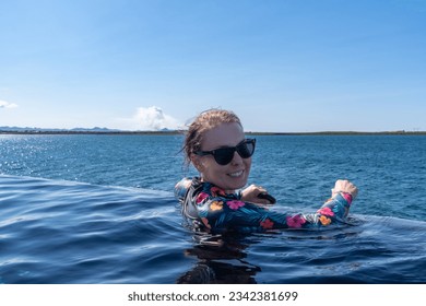 Woman wearing a rashguard at the infinity pool sky lagoon, in Iceland, as a volcano erupts in the background - Shutterstock ID 2342381699