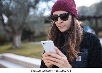 Woman Wearing Red Beanie And Sunglasses Using A Mobile Phone Outdoor

