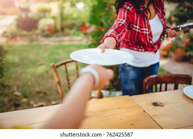Woman wearing red plaid shirt placing dishes on the table at backyard patio