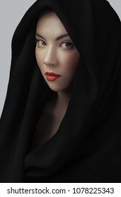 Woman Wearing Scarf With Hood. Beautiful Woman Big Eyes Covers Her Face With A Black Cloth. Red Lips Girl Under Hood. Isolated On Gray Background