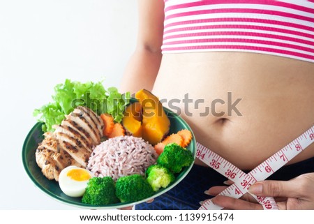 Woman wearing sport bra with belly fat and measuring tape holding a dish of healthy food. Healthy and Diet concept