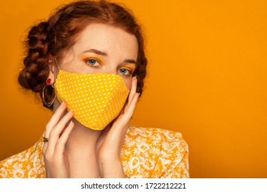 Woman wearing stylish handmade protective face mask posing on orange background.  Model with colorful eyes makeup. Fashion during quarantine of coronavirus outbreak. Copy, empty space for text