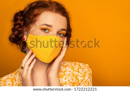 Woman wearing stylish handmade protective face mask posing on orange background.  Model with colorful eyes makeup. Fashion during quarantine of coronavirus outbreak. Copy, empty space for text