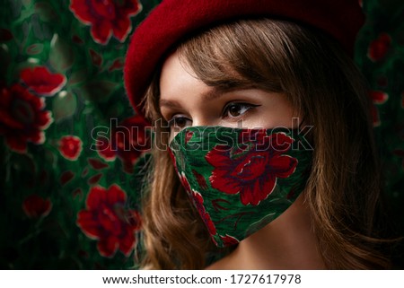 Woman wearing stylish handmade protective face mask posing on matching background of the same cloth. Fashion during quarantine of coronavirus outbreak