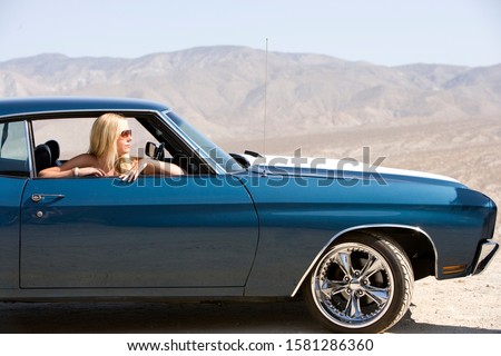 Woman wearing sunglasses driving classic car on road trip in desert
