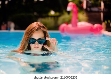 Woman wearing sunglasses in a pool with pink flamingo float in the background