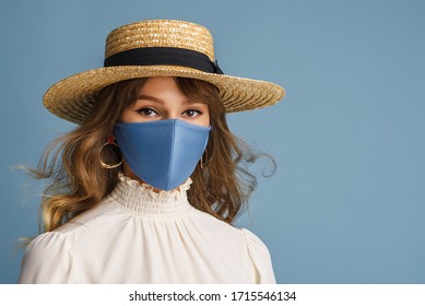 Woman wearing trendy spring, summer fashion outfit during quarantine of coronavirus outbreak. Model dressed protective stylish handmade face mask, straw hat, white blouse, earrings. Copy, empty space