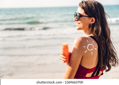 Woman wearing two piece bikini applying suncream with sun drawn on back on the tropical beach.Summer vacations