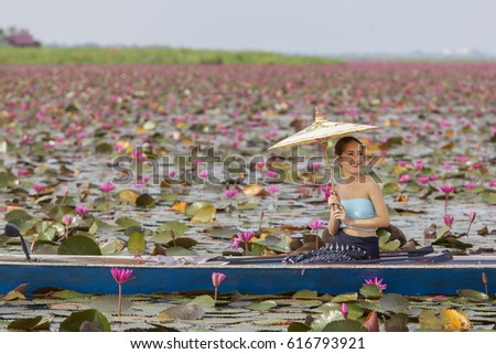 Woman wearing typical Lao dress with umbrella sitting on the boat in red lotus lake.