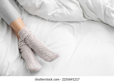 Woman wearing warm socks in comfortable bed, closeup. Space for text