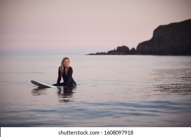 Woman Wearing Wetsuit Sitting And Floating On Surfboard On Calm  Sea