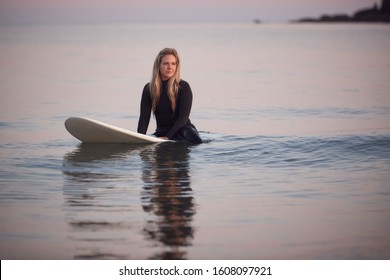 Woman Wearing Wetsuit Sitting And Floating On Surfboard On Calm  Sea