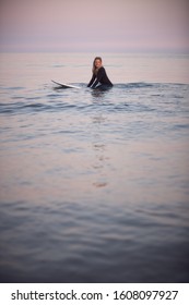 Woman Wearing Wetsuit Sitting And Floating On Surfboard On Calm  Sea