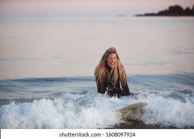 Woman Wearing Wetsuit Sitting On Surfboard Riding Wave Into Beach