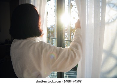 Woman wearing white bathrobe standing at morning near window in the light room - Shutterstock ID 1488474599