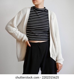Woman wearing white chunky cardigan, striped t shirt and black trousers isolated on white background.