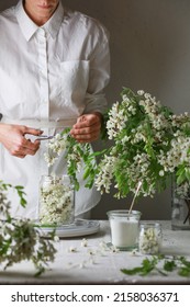 Woman wearing in white dress put acacia flowers in a jar. Girl prepares acacia jam.
