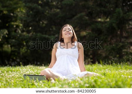 woman wearing white dress sitting on grass in park with netbook