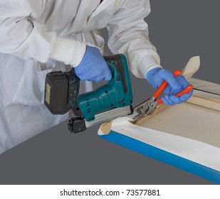 Woman wearing a white lab coat and protective nitrile gloves while stretching canvas fine art photograph print using canvas stretcher pliers and staple gun.