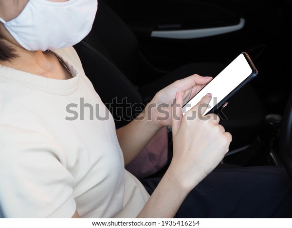A woman wearing a white mask Playing\
a mobile smartphone with a white screen while\
driving