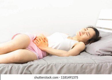 woman wearing white and pink clothes on bed, holding hand to belly pain area,She has abdominal pain,stomachache, health care concept