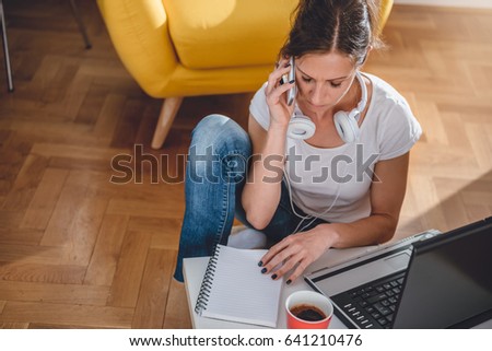Woman wearing white shirt sitting at the coffee table and talking on the smart phone at home