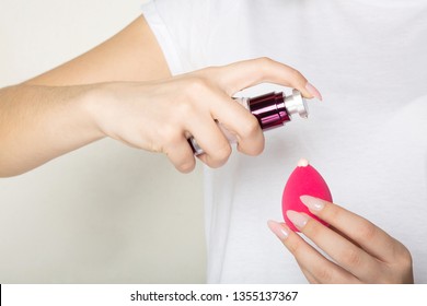 Woman wearing white t shirt applying liquid foundation on a makeup sponge. Closeup shot