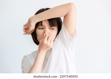 A woman wearing a white t-shirt expressing disgust at the smell of her armpits.