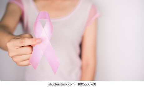 Woman wearing a white t-shirt is hand holding pink ribbon with white background, Breast cancer symbol, Breast cancer awareness month. Important days in October - Shutterstock ID 1805503768